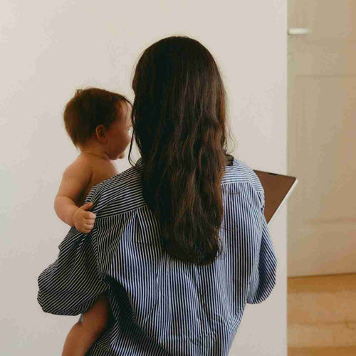 Woman holding a baby in a room with a white wall and wooden floor.