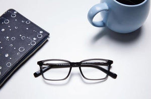 Black eyeglasses with notebook and coffee cup on white surface