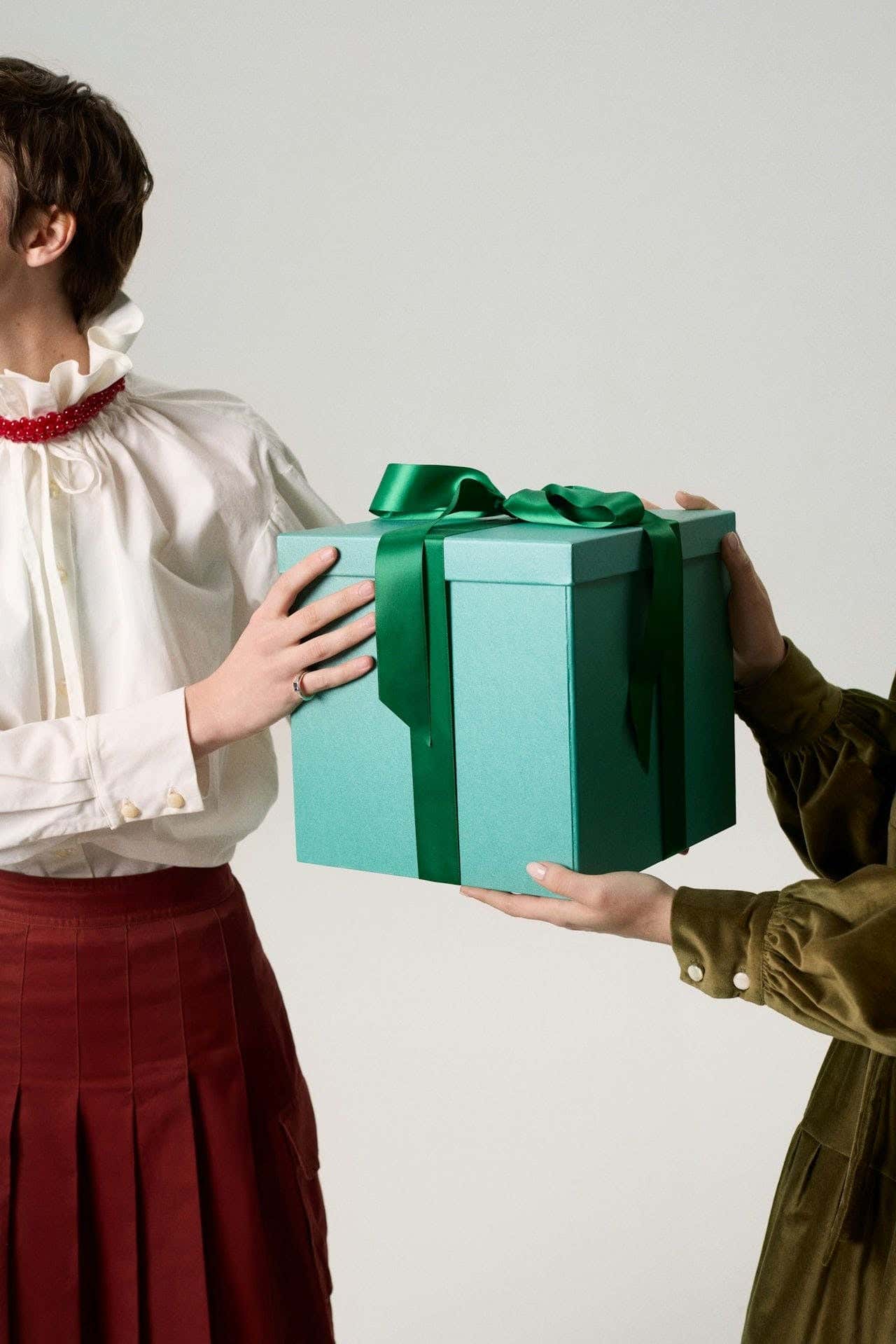 hands holding teal gift box with green ribbon