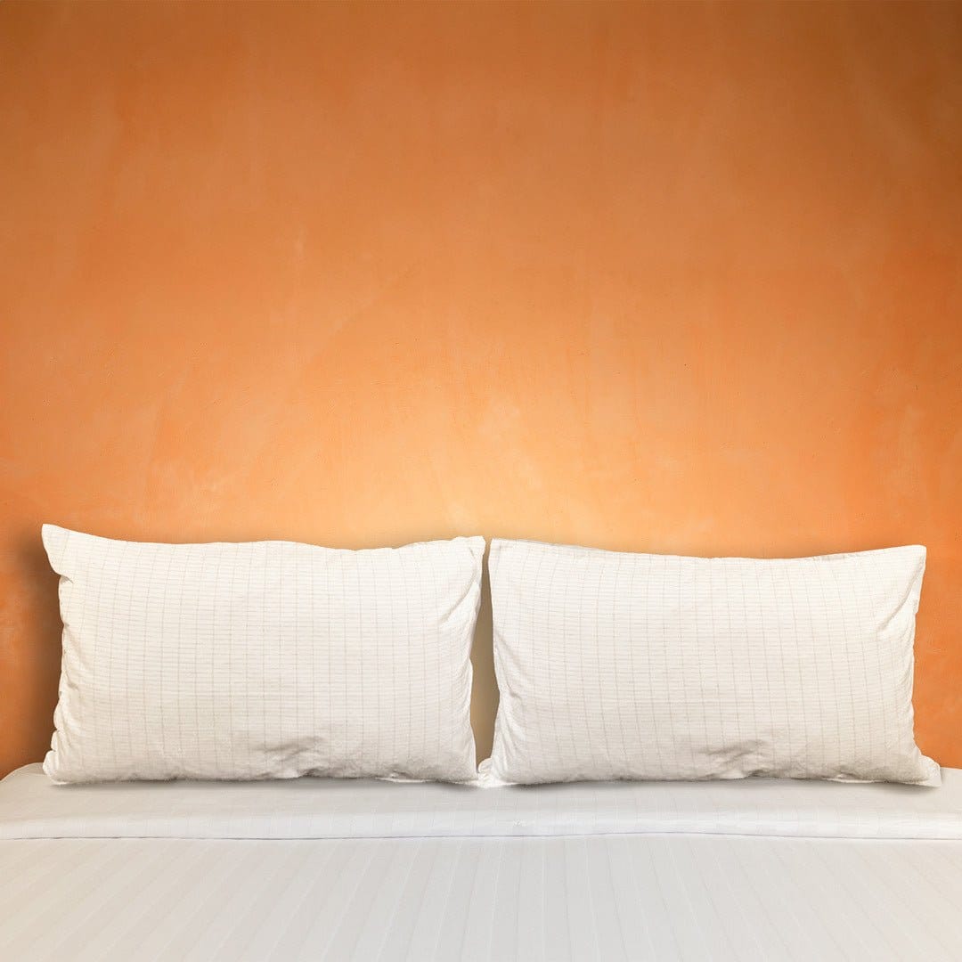 Two white pillows on bed with orange wall