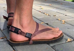 Person's feet wearing brown sandals on pavement.