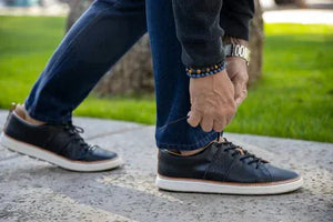 Man tying black leather shoe on sidewalk