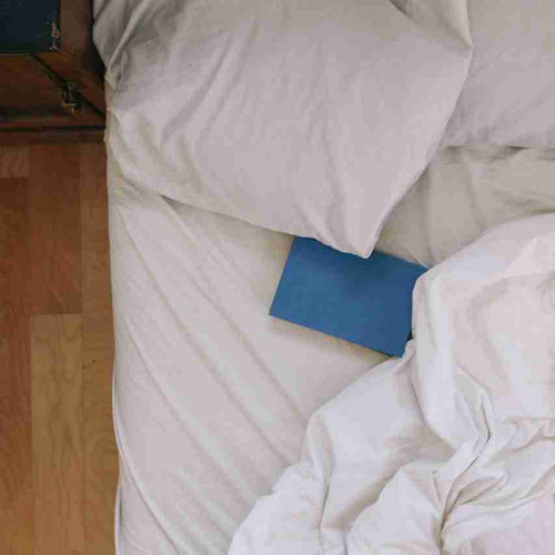 Blue book on a white bed with wooden floor.