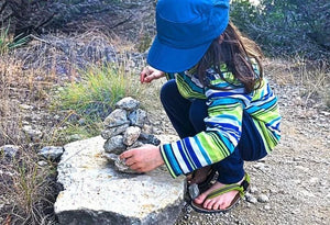 Child in green sandals building rock cairn